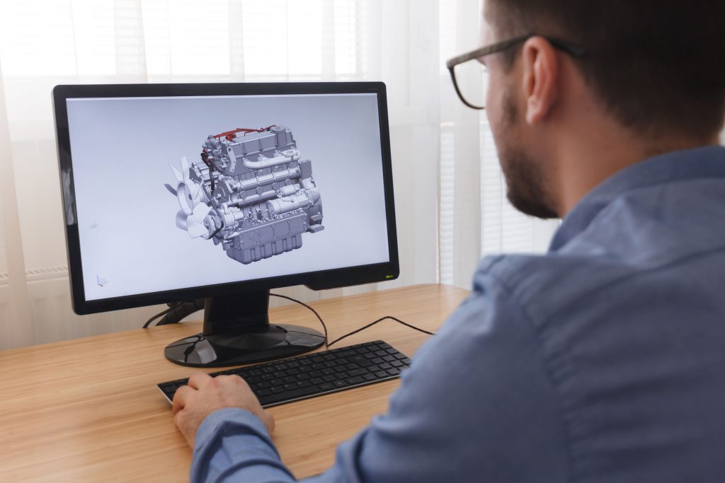 Visualization services - Engineer, Constructor, Designer in Glasses Working on a Personal Computer. He is Creating, Designing a New 3D Model of Car Engine, Motor in CAD Program. Freelance Work.
